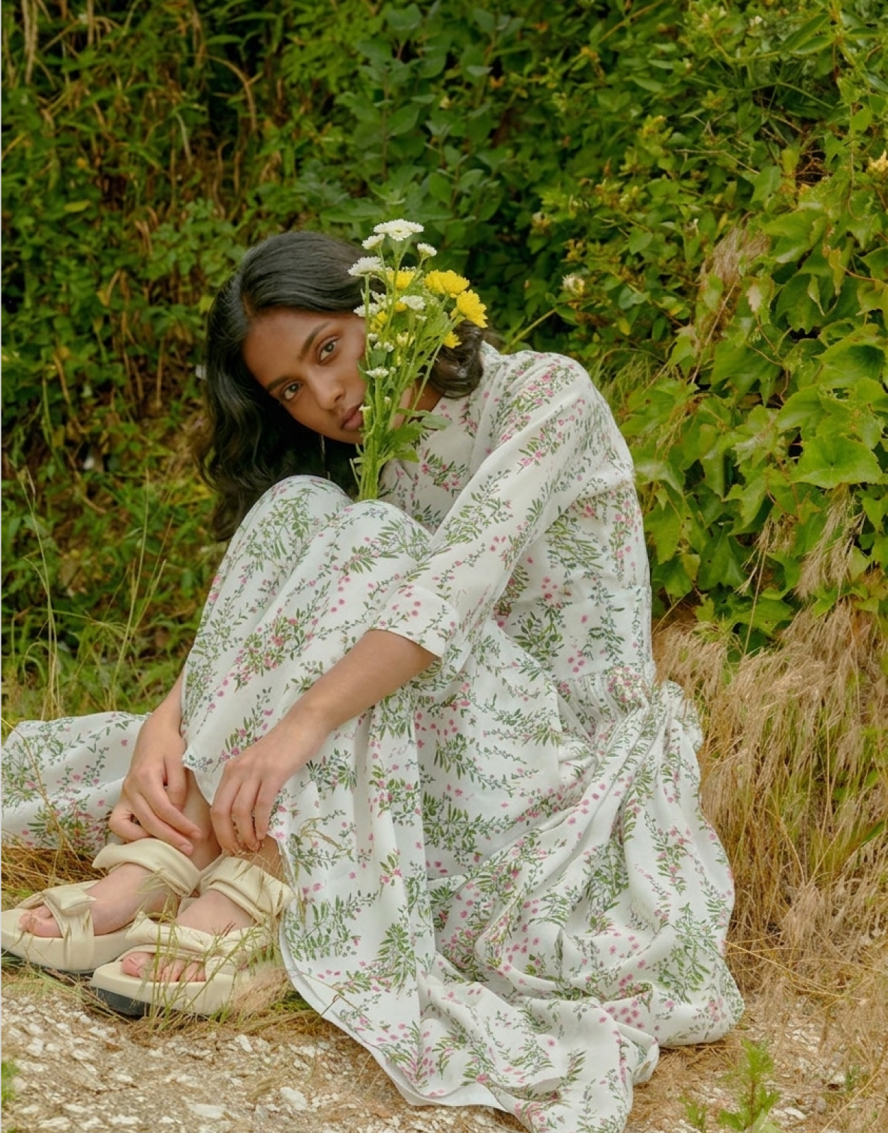 2019 collection — a floral sheer dress seated on a stone path in tall grass
