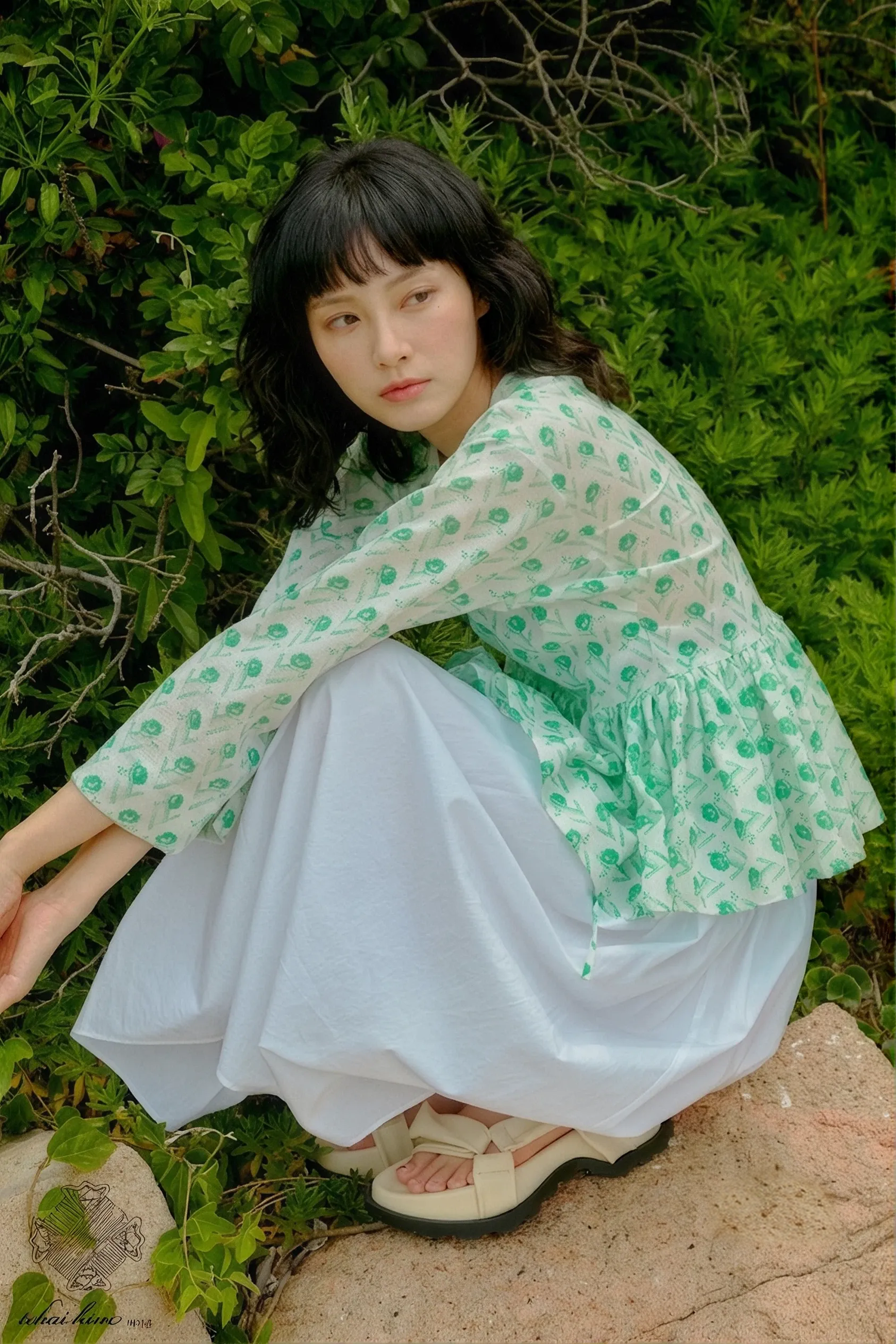 A model in a green floral jeogori seated among summer greenery