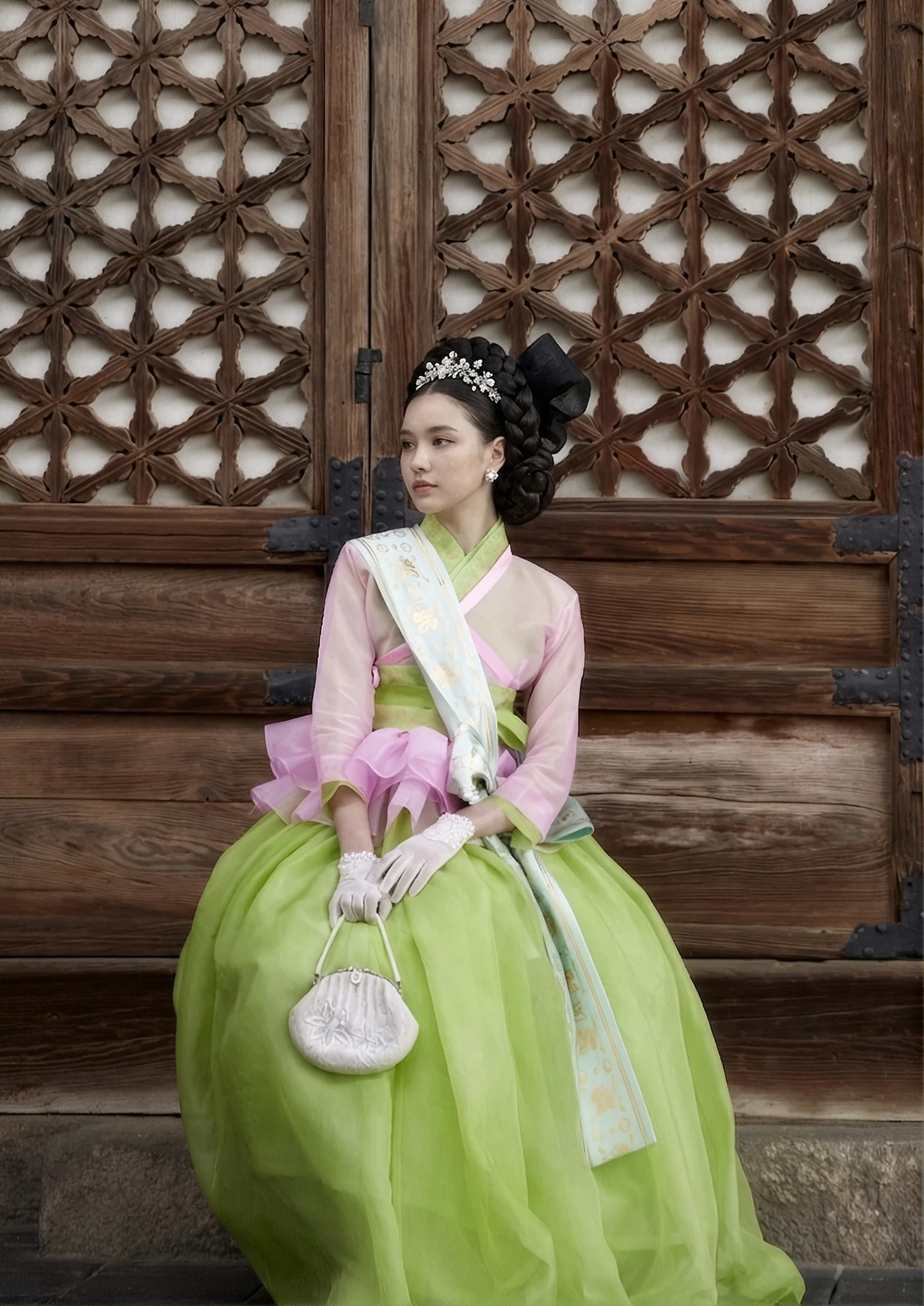 2021 collection — a pink jeogori and chartreuse skirt seated at a carved palace lattice door