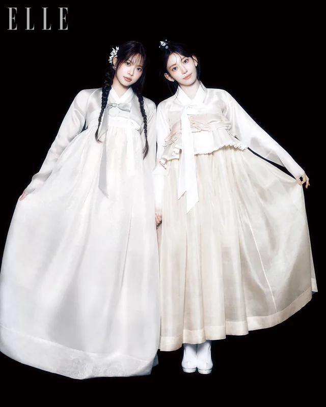 Two women wearing white contemporary hanbok against a black background