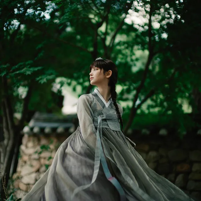 A woman wearing a grey hanbok in a shaded garden