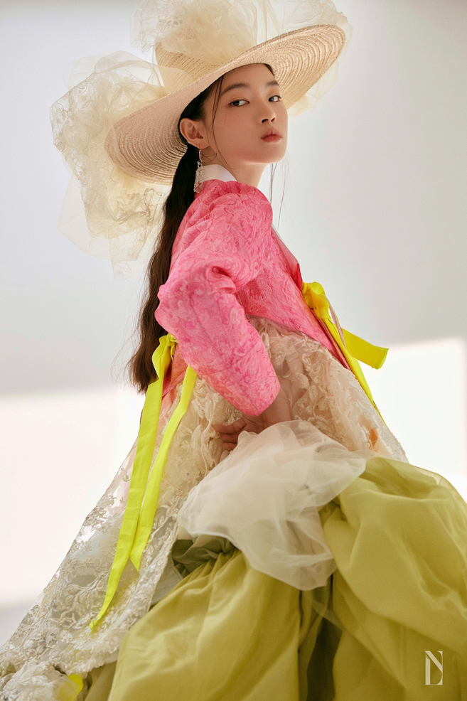 A model wearing a vivid pink couture hanbok and a wide woven hat