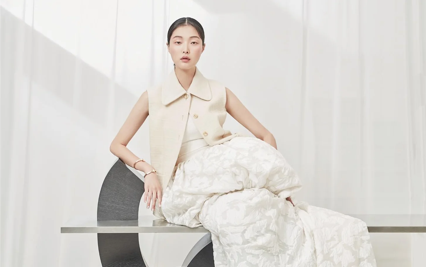 A model in a Tchai Kim vest and skirt seated by a window