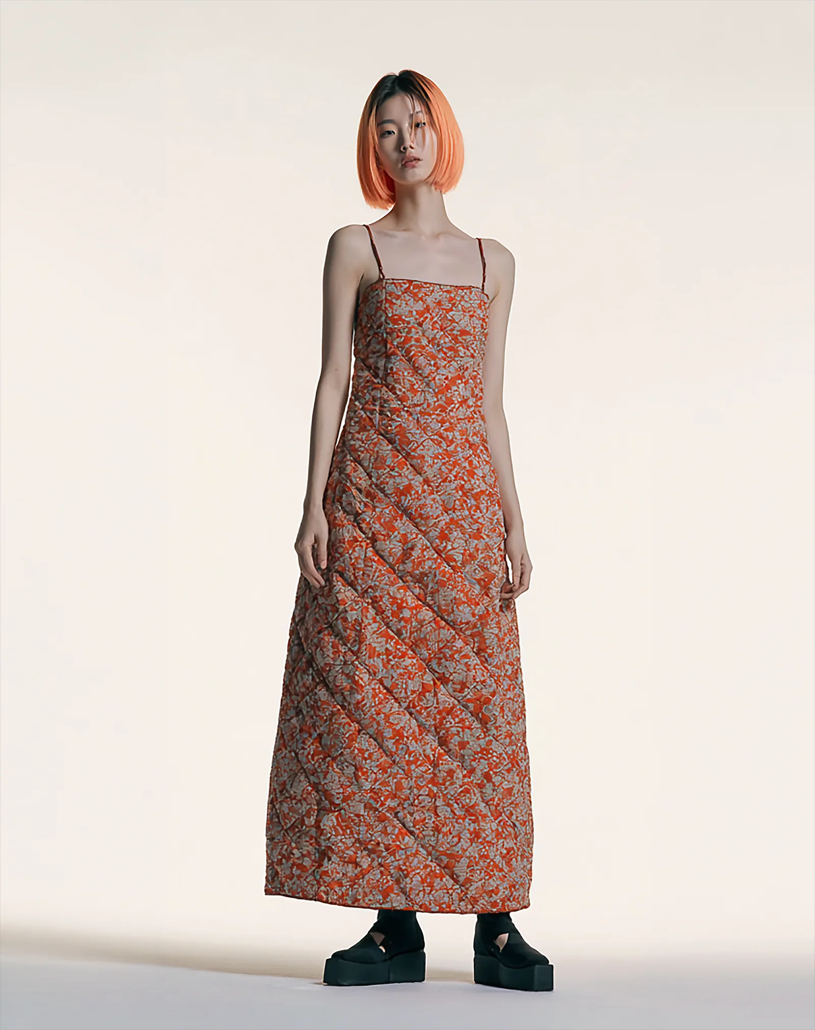 A model wearing the Flower Chess Geodeul Sundress, a column-length dress with diagonal panel lines and a vivid floral-check motif