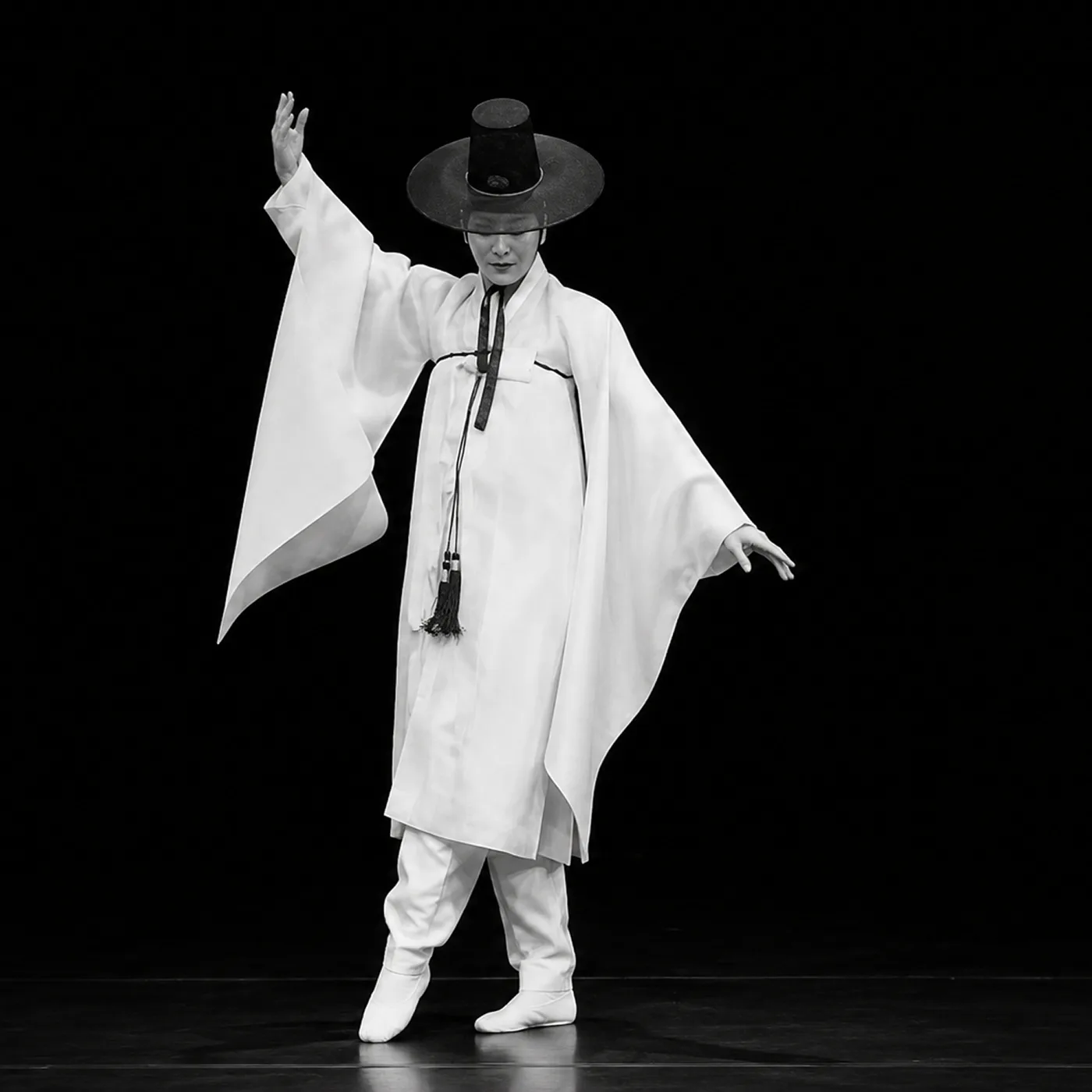 A Namsadangpae performer in white robes and a wide-brimmed hat, one arm raised mid-performance